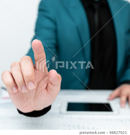 Businessman in Blue jacket sitting at table And Pointing With One Finger On Important Message. Gentleman Showing Critical Announcement. Phone on table. 98627021
