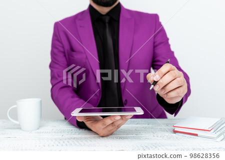 Man in Pink jacket sitting at white table And Pointing With Pen On Important Message. Holding mobile phone. Gentleman Showing Critical Announcement. Man in Pink jacket sitting at white table And Pointing With Pen On Important Message. Holding mobile phone. Gentleman Showing Critical Announcement. 98628356
