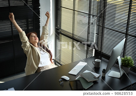 Happy business woman in formal suit outfit stretching arms, relaxing on comfortable office chair in modern office workplace 98628553