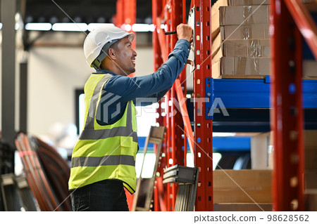 Side view of warehouse worker checking goods and supplies on shelves in large warehouse distribution center environment 98628562