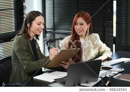 Smiling business colleagues talking and examining financial reports at modern workplace 98628563