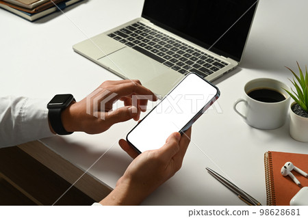 Cropped image of businessman sitting front of laptop at his workstation and using smart phone Cropped image of businessman sitting front of laptop at his workstation and using smart phone 98628681