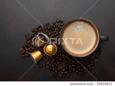 Large cup of coffee with raw beans and ground coffee capsules on brown Large cup of coffee with raw beans and ground coffee capsules on brown 98629652