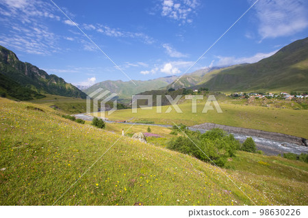 A beautiful mountain landscape with a small meandering river and a blue sky. Mountainous Georgia. A beautiful mountain landscape with a small meandering river and a blue sky. Mountainous Georgia. 98630226