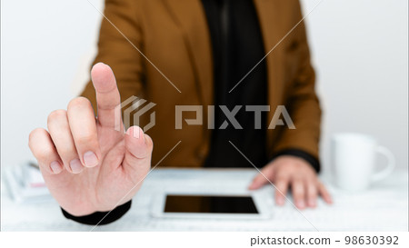 Businessman in Brown jacket sitting at table And Pointing With One Finger On Important Message. Gentleman Showing Critical Announcement. Phone on table. 98630392