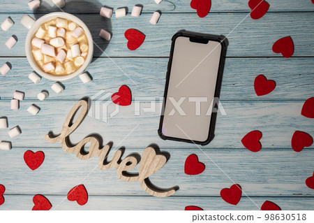 Greeting or invitation white screen on mobile phone mock up with white cup of coffee and marshmallows on wooden background. Romantic Small hearts Valentine day. Blank card copy space for your text. Greeting or invitation white screen on mobile phone mock up with white cup of coffee and marshmallows on wooden background. Romantic Small hearts Valentine day. Blank card copy space for your text. 98630518