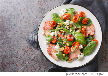 Warm french salad with bacon, spinach, roquefort cheese, walnuts, tomatoes, basil and garlic close-up in a plate. Horizontal top view 98634628