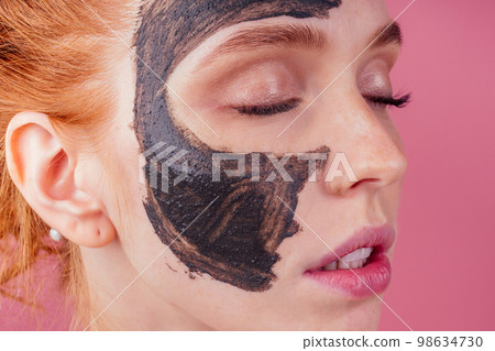 redhaired ginger teenager girl with black clay mask on her pretty face on pink studio background redhaired ginger teenager girl with black clay mask on her pretty face on pink studio background 98634730