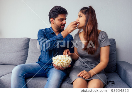 Portrait of romantic positive indian couple in apartment living room having plate of chips snack enjoying time together 98634833