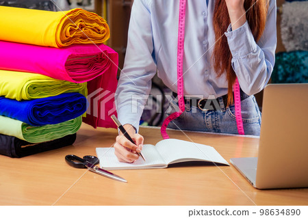 tailor small business idea.redhaired ginger woman in cotton shirt stand in her dressmaking atelier studio 98634890