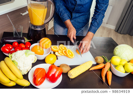 young indian man in the kitchen prepares a fresh orange juice 98634919
