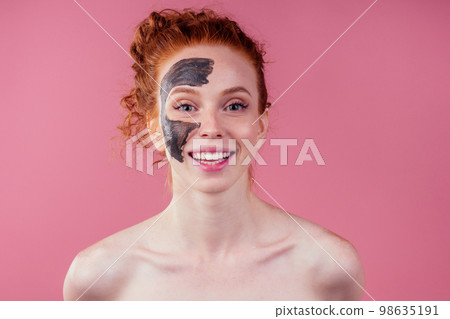 redhaired ginger teenager girl with black clay mask on her pretty face on pink studio background redhaired ginger teenager girl with black clay mask on her pretty face on pink studio background 98635191