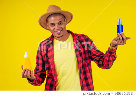 afro brazilian man choosing spf bottle in studio yellow wall 98635198