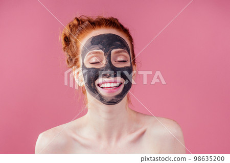 redhaired ginger teenager girl with black clay mask on her pretty face on pink studio background 98635200