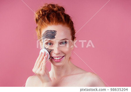 redhaired ginger teenager girl with black clay mask on her pretty face on pink studio background redhaired ginger teenager girl with black clay mask on her pretty face on pink studio background 98635204