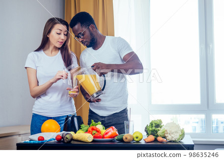 african american man with asian woman making smoothie at home, useing eco tubes from metall african american man with asian woman making smoothie at home, useing eco tubes from metall 98635246