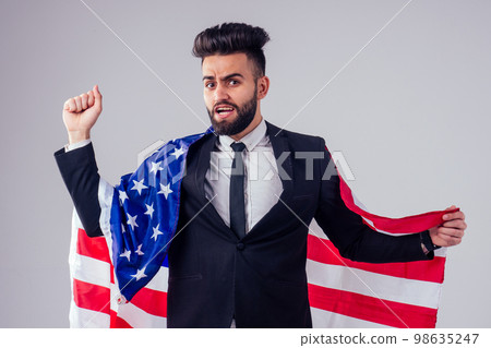arabian young handsome black hair man in stylish business suit holding american flag in studio isolate white background.Independence Day concept 98635247