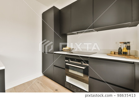 a modern kitchen with black cabinets and white countertops on the wall, an oven is in the center of the room 98635413