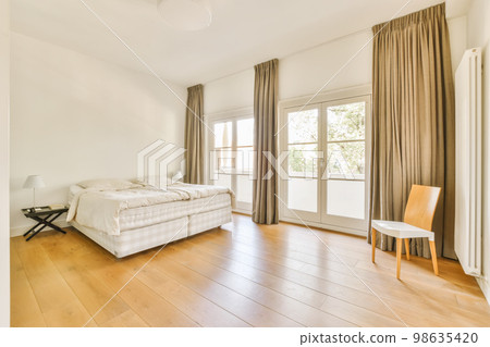 a bedroom with wood flooring and white walls, including a large bed in the room is surrounded by beige drapes 98635420
