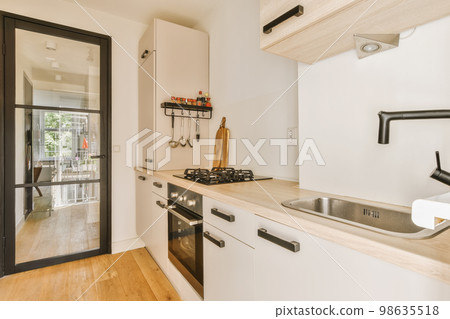 a kitchen with wood flooring and white cupboards, black door handles, and an oven in the corner 98635518