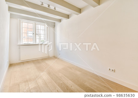 an empty room with white walls and wood flooring on one side, there is a small window in the corner 98635630