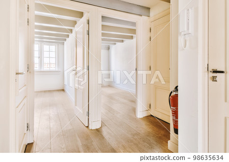 an empty room with white walls and wood flooring on the right side, there is a red fire exor in the door an empty room with white walls and wood flooring on the right side, there is a red fire exor in the door 98635634
