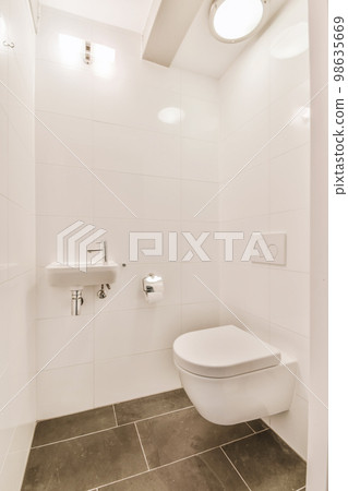 a bathroom with white walls and tile flooring, including a toilet in the center of the photo is a wall mounted mirror a bathroom with white walls and tile flooring, including a toilet in the center of the photo is a wall mounted mirror 98635669