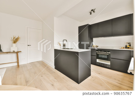 a modern kitchen with black cabinets and white countertops on the island in an open plan living room is also visible a modern kitchen with black cabinets and white countertops on the island in an open plan living room is also visible 98635767