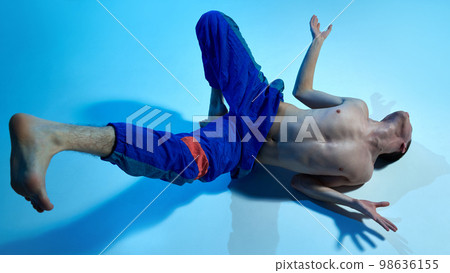 Contemporary dance style. Young artistic man dancing contemp, experimental dance over blue studio background. Expressive feelings 98636155
