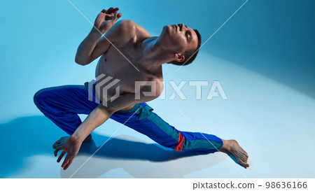 Contemporary dance style. Young shirtless man dancing, performing contemp, experimental dance over blue studio background 98636166