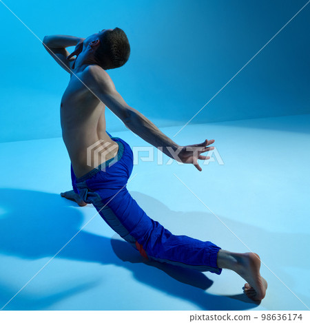Contemporary dance style. Young shirtless man dancing, performing contemp, experimental dance over blue studio background 98636174