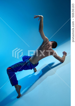 Contemporary dance style. Young shirtless man dancing over blue studio background. Male body art. Contemp, experimental dance 98636183