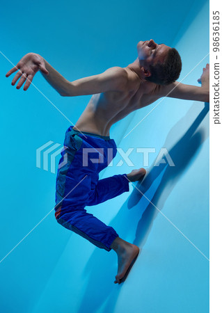 Contemporary dance style. Young shirtless man dancing contemp, experimental dance over blue studio background. Flexibility Contemporary dance style. Young shirtless man dancing contemp, experimental dance over blue studio background. Flexibility 98636185