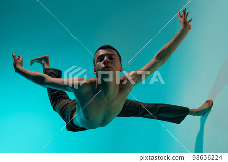 Contemporary dance style. Young shirtless man dancing over blue, cyan studio background. Expressive modern dance Contemporary dance style. Young shirtless man dancing over blue, cyan studio background. Expressive modern dance 98636224