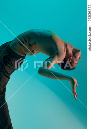 Contemporary dance style. Young flexible shirtless man dancing experimental dance over cyan color studio background. Modern Contemporary dance style. Young flexible shirtless man dancing experimental dance over cyan color studio background. Modern 98636251
