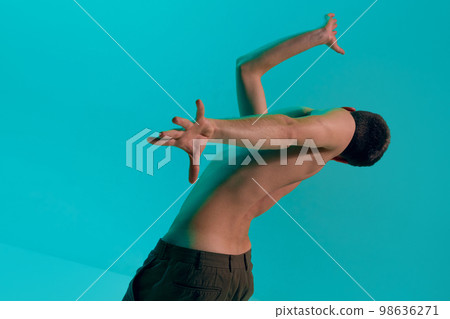 Contemporary dance style. Young shirtless flexible man dancing modern dance over blue, cyan studio background. Self-expression, lifestyle Contemporary dance style. Young shirtless flexible man dancing modern dance over blue, cyan studio background. Self-expression, lifestyle 98636271