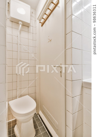 a white toilet in a small bathroom with tile flooring and wall tiles on the walls there is a mirror above it a white toilet in a small bathroom with tile flooring and wall tiles on the walls there is a mirror above it 98636311