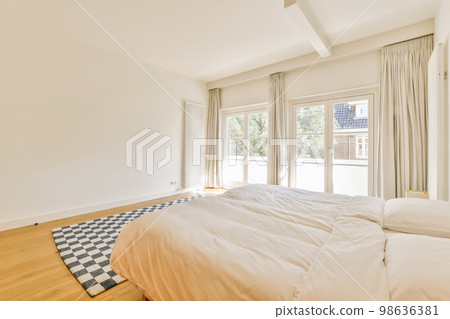 a bedroom with white walls and hardwood flooring in the middle part of the room, there is a large bed 98636381