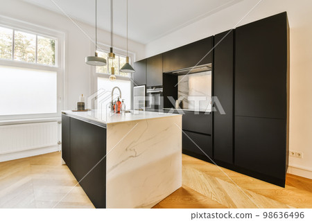 a modern kitchen with black cabinets and white marble countertops in the island is surrounded by wooden flooring boards 98636496