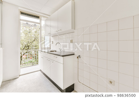 a kitchen area with white tiles on the walls and floor, there is an open door leading to another room a kitchen area with white tiles on the walls and floor, there is an open door leading to another room 98636500