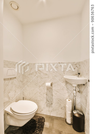a modern bathroom with marble walls and flooring, including a white toilet and black rug in the corner of the room 98636763