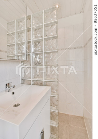 a white bathroom with glass blocks on the wall behind it and a mirror in the shower stall to the right 98637051