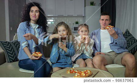 Family watches comedy and enjoys eating pizza at home 98637061