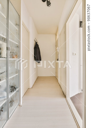 a long hallway with white walls and wood flooring on the right side, there is a coat rack in the left corner a long hallway with white walls and wood flooring on the right side, there is a coat rack in the left corner 98637067