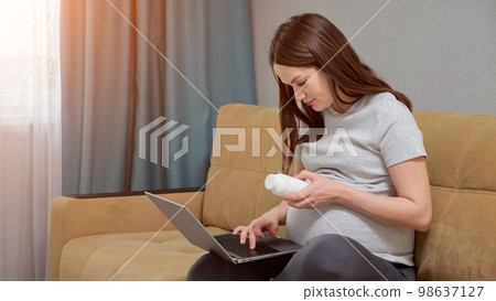 Pregnant woman reads prescription of pills on laptop 98637127