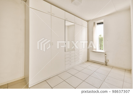 an empty room with white cupboards and floor tiles on the floor, there is a window in the wall 98637307