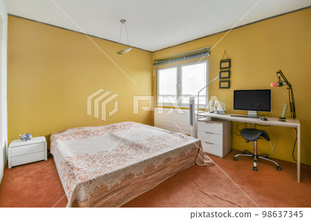 a bedroom with a bed, desk and computer monitor on the wall in front of the window looking out onto the street 98637345