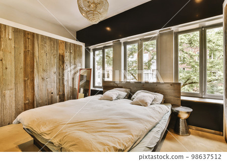 Home interior design of bedroom with bed and wooden wardrobe placed in corner near window in modern apartment 98637512