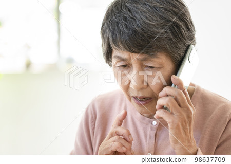 Elderly woman with a grim expression talking on a smartphone Elderly woman with a grim expression talking on a smartphone 98637709