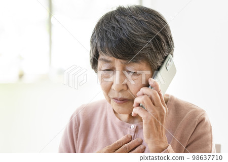 An elderly woman with an uneasy expression talking on a smartphone 98637710